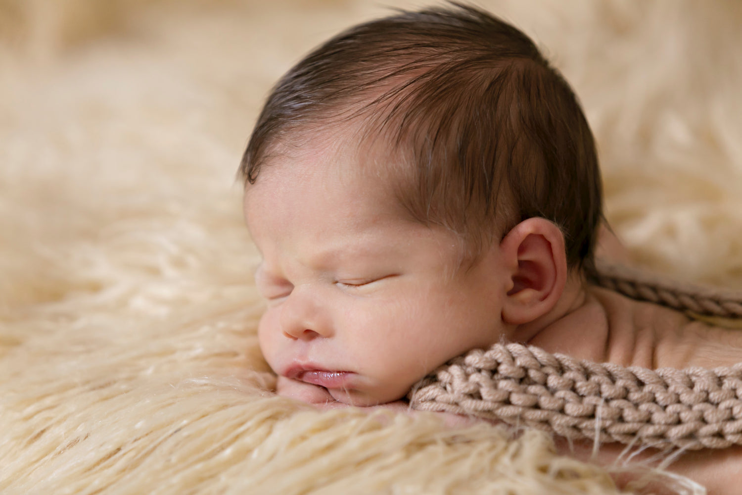 Neugeborenes Baby mit dunklen Haaren liegt auf einem Lammfell